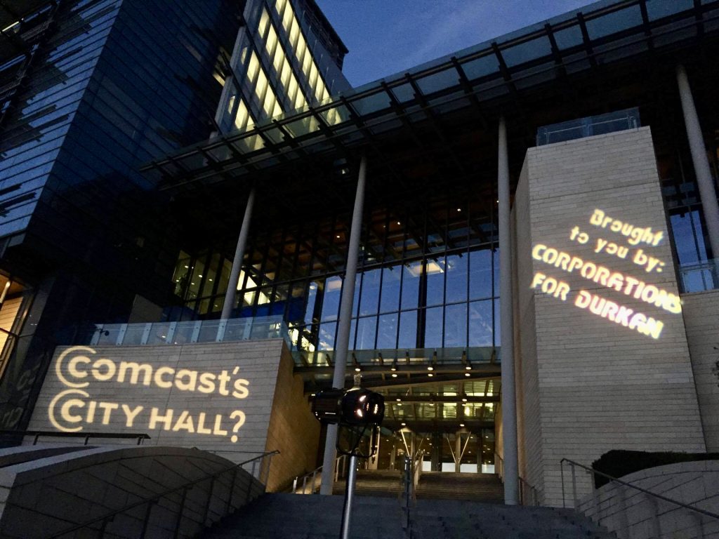 A photo of Seattle's city hall with the text "Comcast's city hall" projected by a light. 