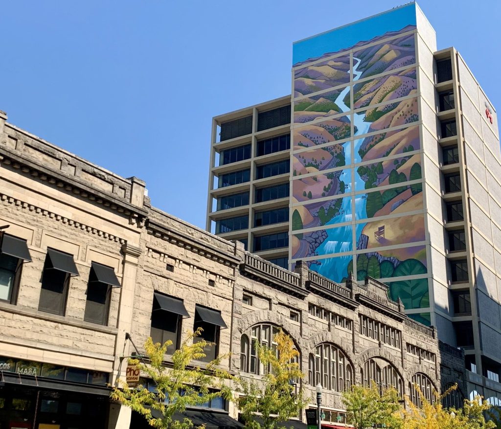 A photo of a mural showing mountains with a river running through them on a tall building.