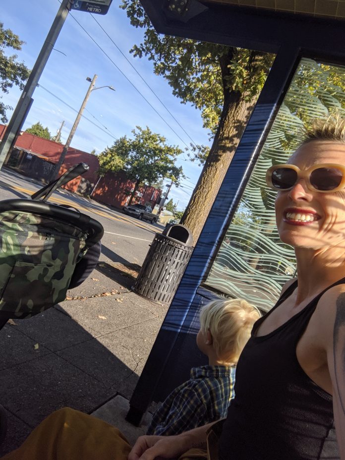 Anna smiles taking a selfie sitting next to her son at a bus stop shelter.