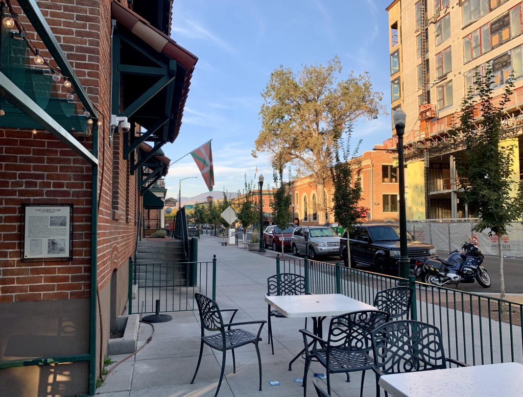 A photo shows an outdoor cafe with tables and chairs. A Basque flag is hung on the building. Across the street a new taller building is under construction. 