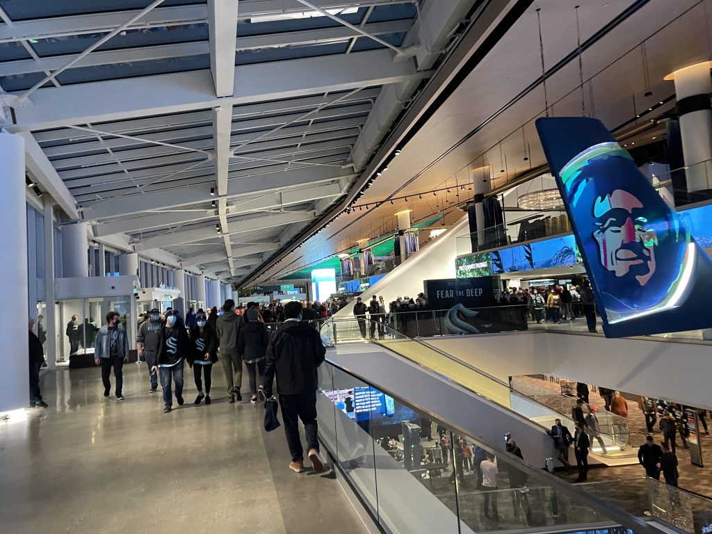 A photo shows people walking inside a stadium near an escalator. 