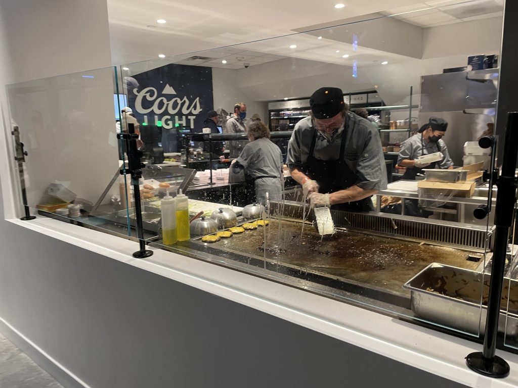 A photo shows a man cooking food on a large flat grill in a concessions stand. 