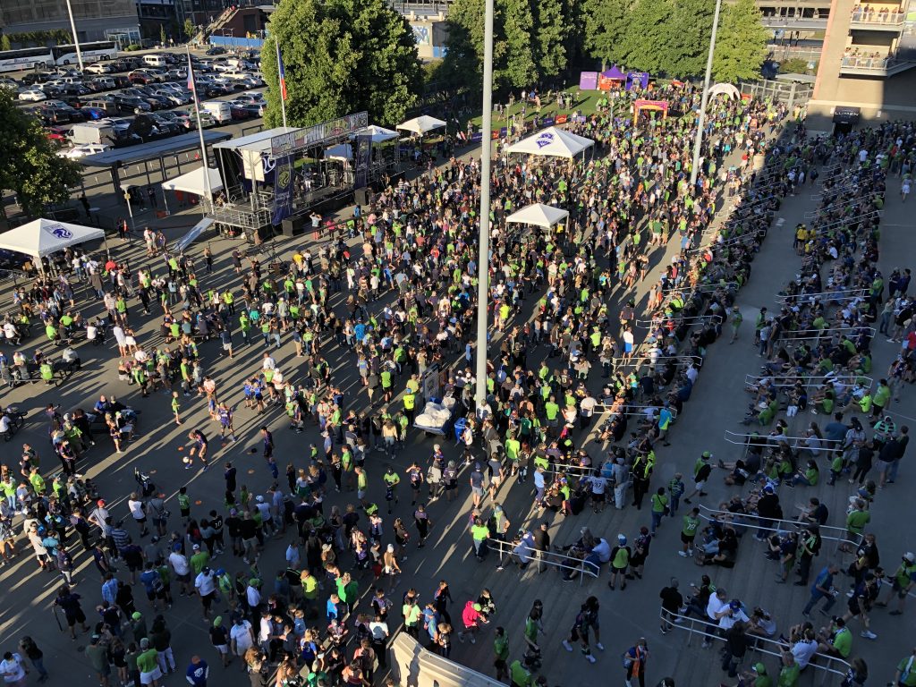 A photo of a crowd of people gathered outside, many of them wearing Seattle Sounders gear. 