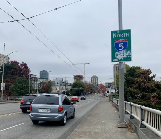 SDOT Drops Protected Bike Lane from NE 45th Street Bridge Plans, Citing Traffic Impacts A photo shows a sidewalk next to a roadway with cars. A sign says North Interstate 5.