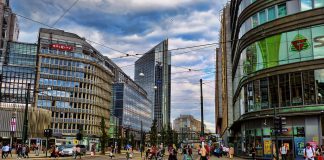 A photo of a city street without cars. There are tram lines and people walking and biking.