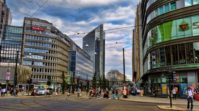 A photo of a city street without cars. There are tram lines and people walking and biking.