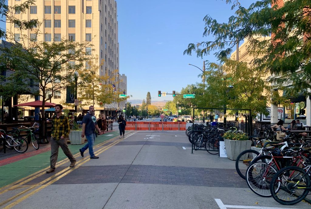 A photo of a pedestrian street with bikes parked on the right side, two men walking on the left, and buildings visible in the distance.