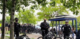 Three bike-wielding cops form a barricade around a sweep with a large contingent of officers behind