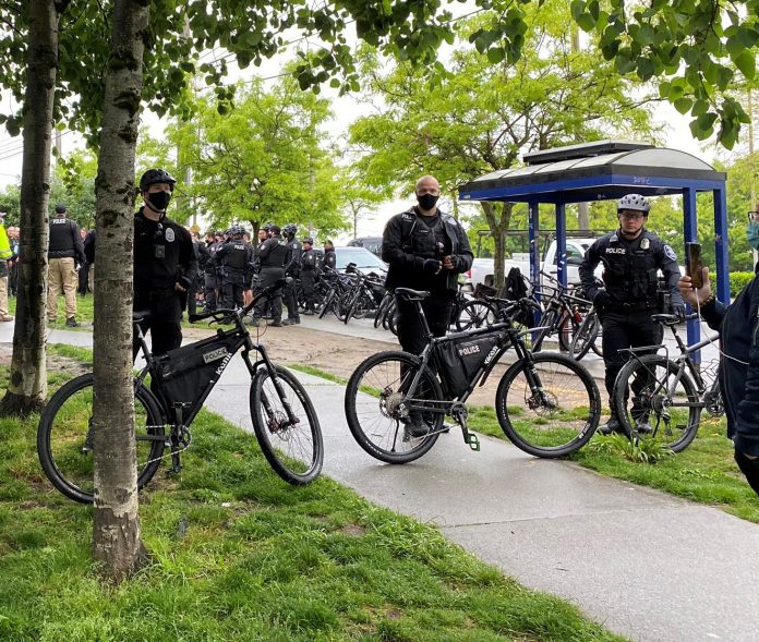 Three bike-wielding cops form a barricade around a sweep with a large contingent of officers behind