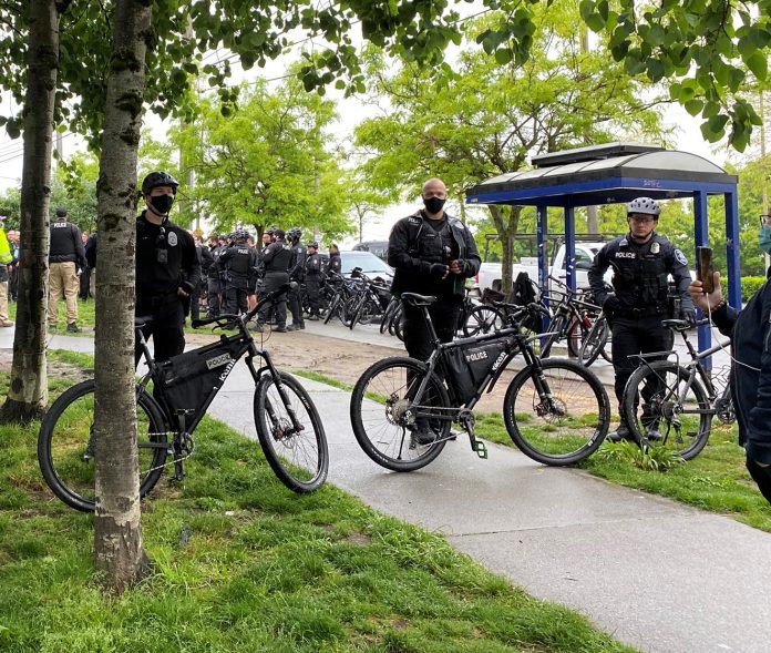 Police barricade during sweep Three bike-wielding cops form a barricade around a sweep with a large contingent of officers behind