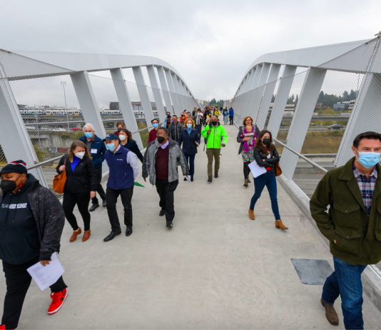 John Lewis Memorial Pedestrian Bridge Partially Mends Freeway Gash in Northgate A photo of people walking on a pedestrian bridge over Interstate 5.
