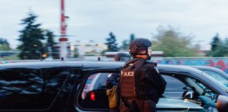 A photo shows a police officer in riot gear standing next to a patrol car.