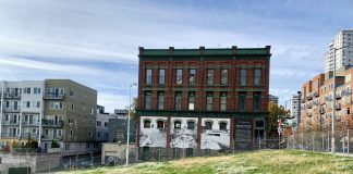 A photo of a green field with a chainlink fence and brick building with a white mural in the background.