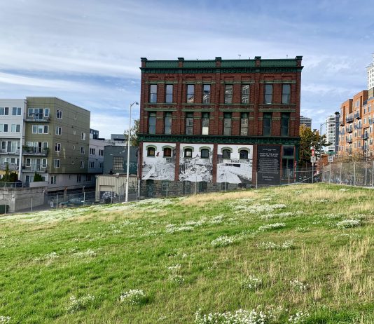 Former Battery Tunnel Site Gets Green Light for Downtown School A photo of a green field with a chainlink fence and brick building with a white mural in the background.