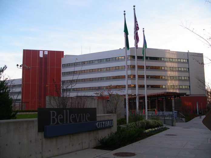 A photo of a modern grey and red building with three flags in front of it.