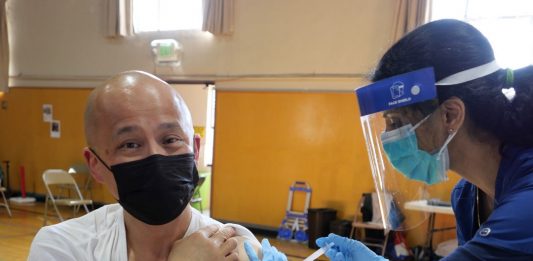 A health worker vaccinates a man wearing a face mask in a gymnasium.