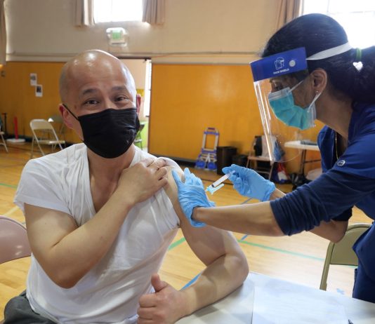 Vaccination Surge Shows Employee Mandates Work A health worker vaccinates a man wearing a face mask in a gymnasium.