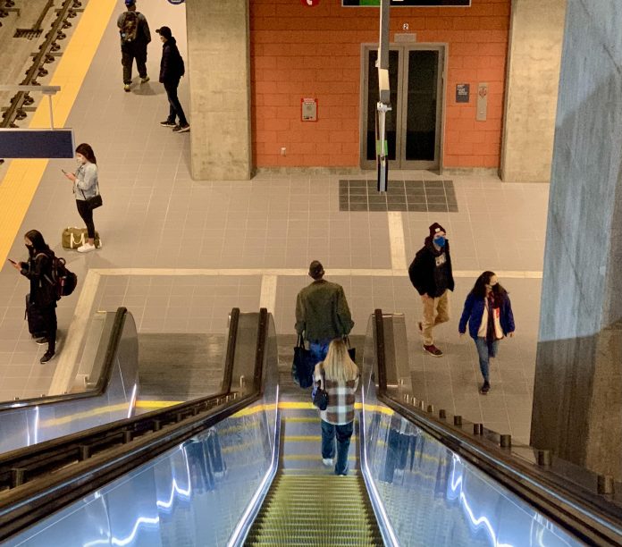 A photo of an illuminated escalator leading down to a light rail platform.