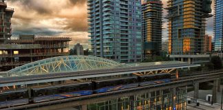 A photo of a light rail station surrounded by tall modern buildings, some of which are still under construction.