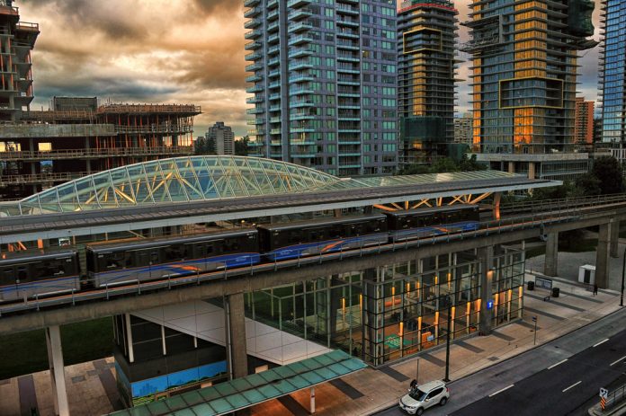 A photo of a light rail station surrounded by tall modern buildings, some of which are still under construction.