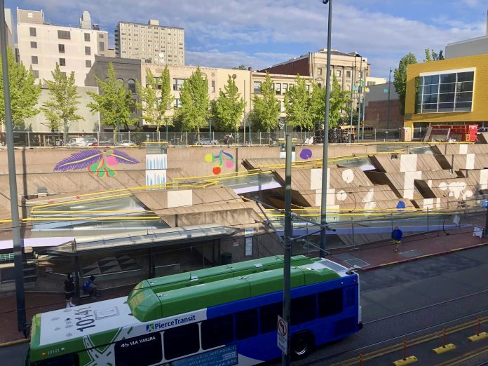 A photo shows a bus in front a public art water feature with brightly colored images painted on cement.