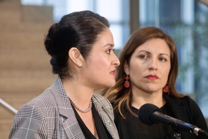 232D71C4-85B1-4CF7-93CF-C65698275AC6_1_201_a Head shot photo of two women in professional attire at a microphone.