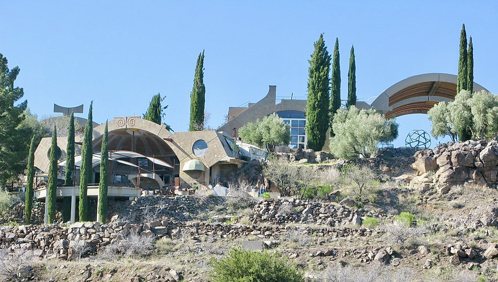 A photo of the some brown curved buildings in the desert with a few trees and shrubs nearby. 
