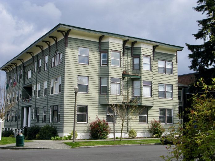 A photo of a light green gray three story apartment building.