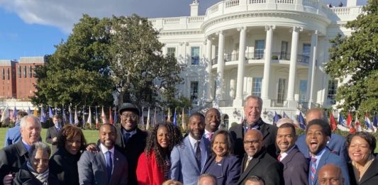 A group of people in business attire pose in from the White House.