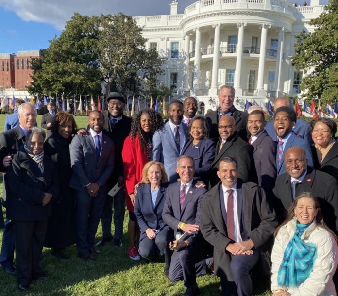 A group of people in business attire pose in from the White House.