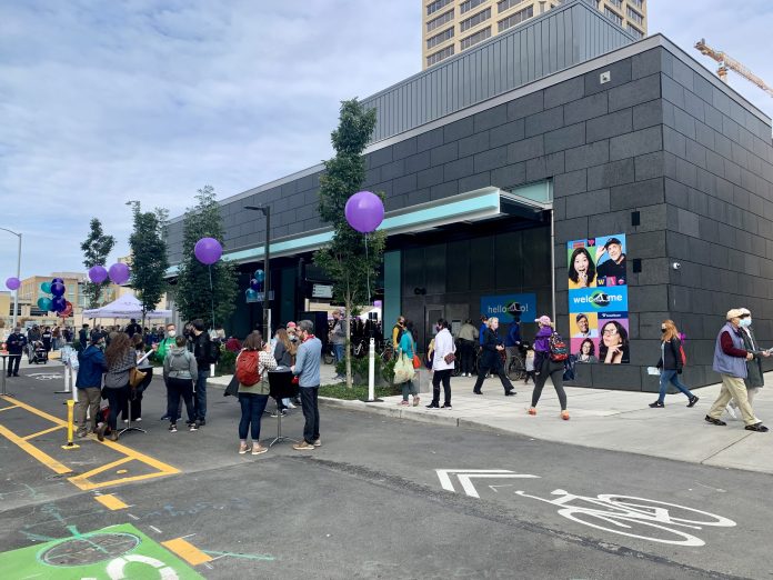 A photo showing people gathered on a street with a bike lane in front the U District light rail station.