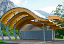 Lecture Series Spotlights Indigenous Architecture A photo of a wave shaped outdoor pavilion made from wood in front of mountains.