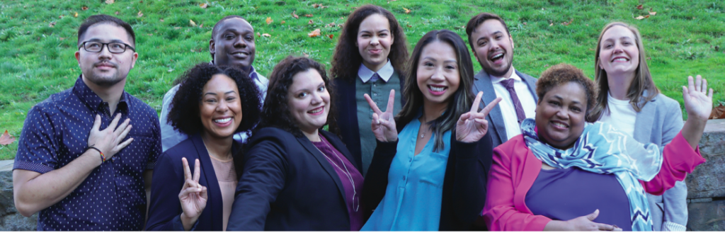A photo of a racially diverse group of adults in professional attire waving and smiling. 