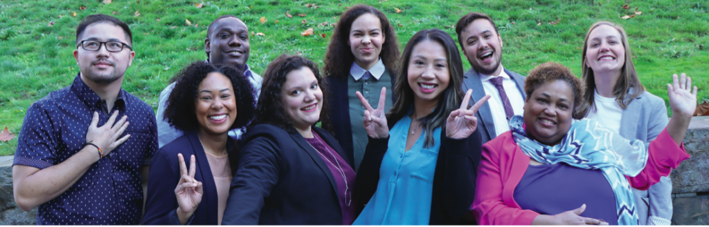 A photo of a racially diverse group of adults in professional attire waving and smiling. 