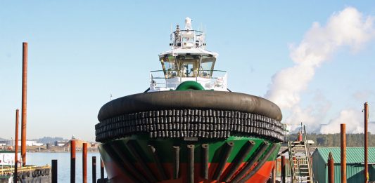 A photo of a black, green, and red tugboat on a platform over the water.