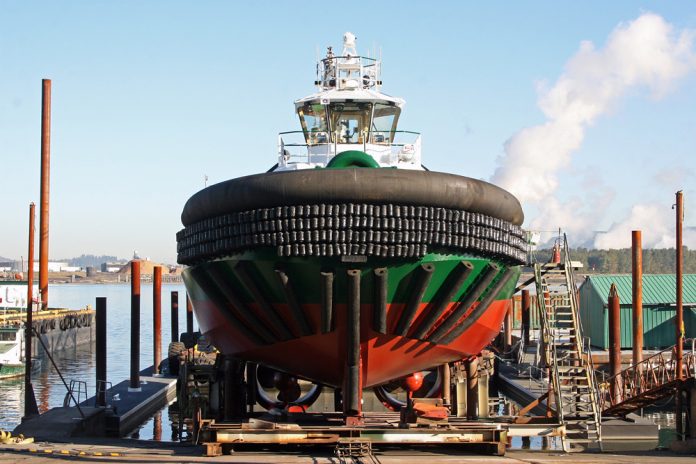 A photo of a black, green, and red tugboat on a platform over the water.