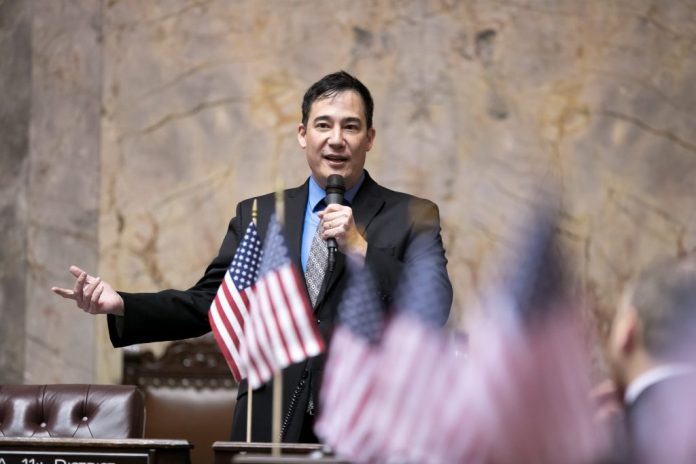 Steve Hobbs on the senate floor with American flags in the foreground.