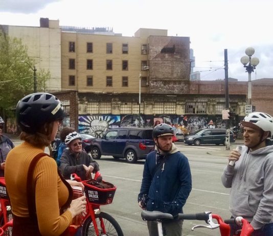 SDOT Director Zimbabwe is Out, What Does This Mean for Seattle Transportation? A group of people wearing bike helmets and standing near bikes listen to a man speaking.
