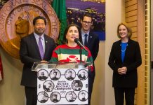 Seattle Council Poised to Appoint Debora Juarez to Vacant D5 Seat Juarez speaks at a podium with a hockey jersey with the City Seal in the background.