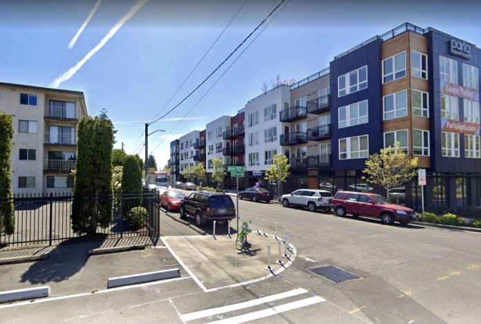 A photo of a street with a crosswalk and curb bulbs near apartment buildings.