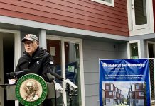 Governor Inslee Backs Fourplex Zoning and $815 Million Push to Reduce Homelessness A photo of a man speaking at a podium decorated with the seal of the State of Washington in front of a townhouse and a sign for habitat for humanity.