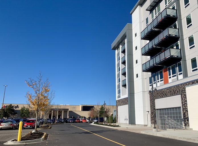 A photo of an apartment next to a parking to with cars and an indoor mall.