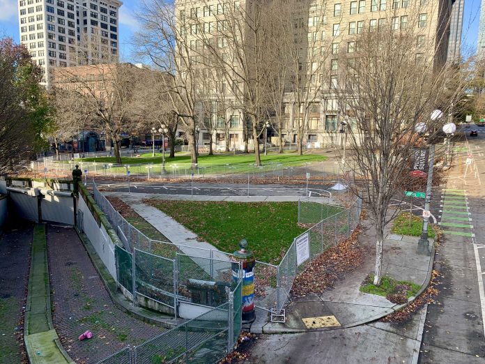 A photo of a green space surrounded by chain link fencing near tall historic buildings