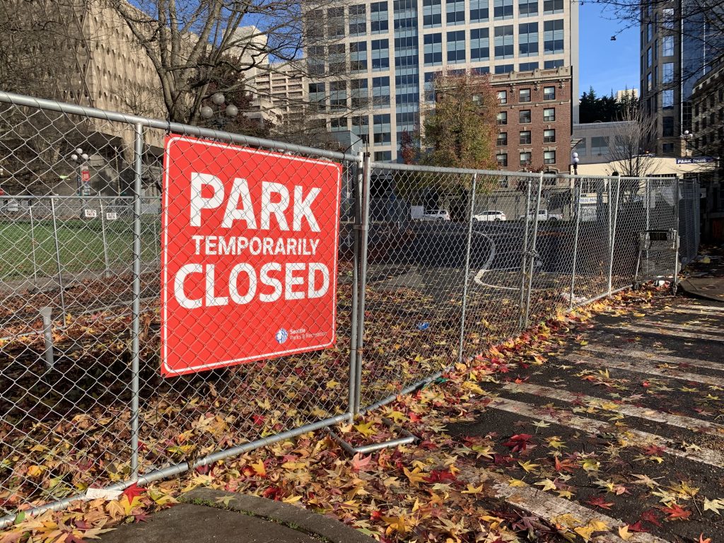 A photo of a chainlink fence and a sign reading "park closed" in front a open grassy area.