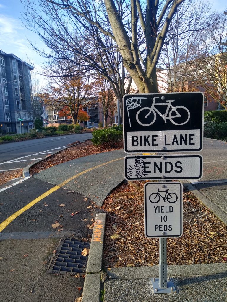 Bike lane ends sign, yield to peds sign with ramp leading to sidewalk