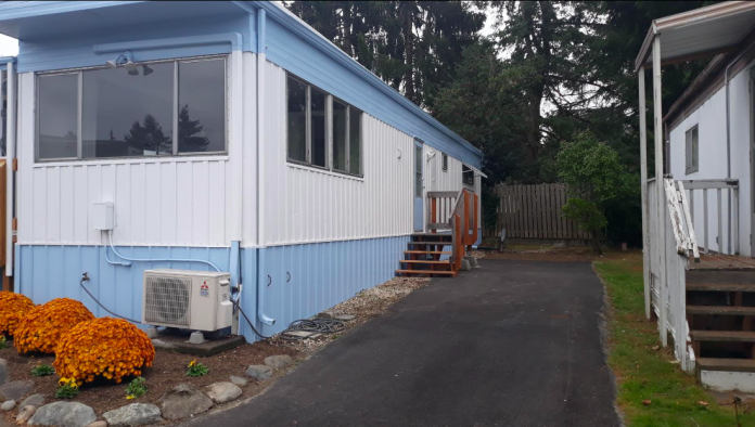 A photo of a light blue and white mobile home with a driveway.