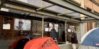 A photo of a tent in front of a glass window with exhibiting large portrait style photos of people.