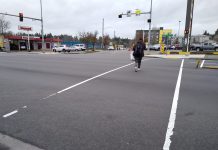 Months After Street Repaving, Lake City Way Crosswalks Still Remain Temporary A wide intersection, with two light white lines and a person crossing with four seconds left on the countdown