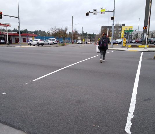 Months After Street Repaving, Lake City Way Crosswalks Still Remain Temporary A wide intersection, with two light white lines and a person crossing with four seconds left on the countdown