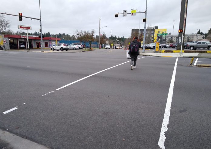 A wide intersection, with two light white lines and a person crossing with four seconds left on the countdown
